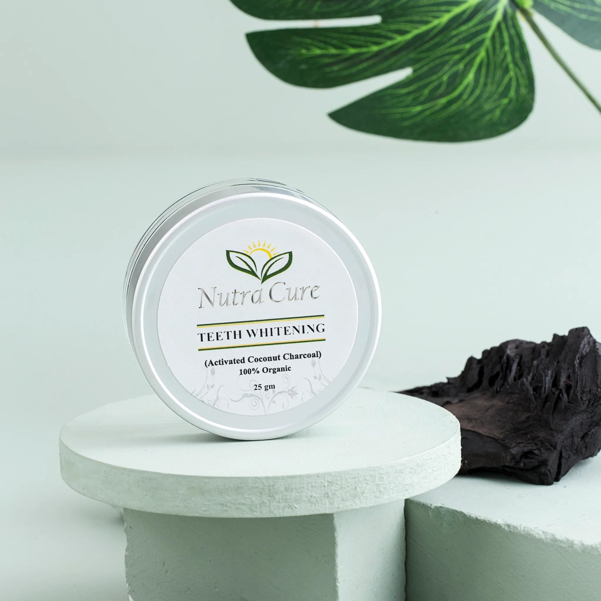 Nutra Cure Organic Activated Charcoal Teeth Whitening Powder jar and product box displayed with natural coconut props and green foliage